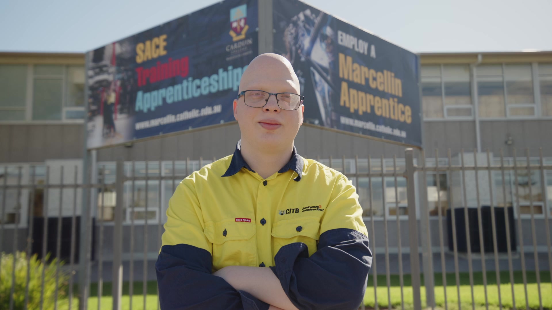 Keagan Wilke in his hi-vis work shirt standing in front of an Employ a Marcellin Apprentice banner